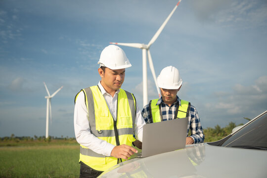 Renewable energy maintenance. Engineer using laptop computer checking system of wind turbine at windmill field farm station. Wind turbine energy storage system. Workers meeting to check around the are