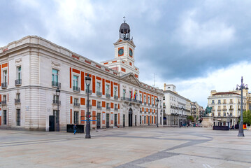 The historic Real Casa de Correos in Madrid's Puerta del Sol, featuring its iconic clock tower, red brick and white stone facade, and Spanish and EU flags flying from the central balcony