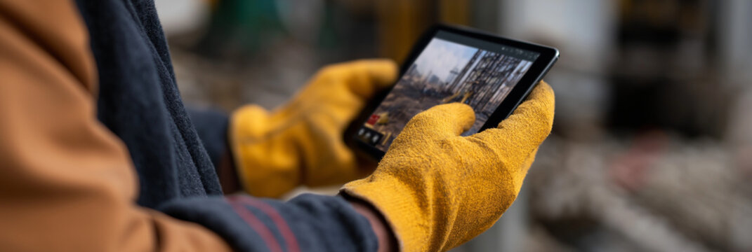 A worker in gloves interacts with a tablet on a construction site, demonstrating modern technology's role in enhancing productivity and safety in rugged environments.