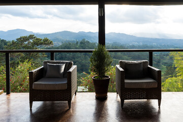 balcony or terrace with two wicker chairs and a potted plant, overlooking a mountainous landscape.