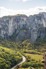 Imposing Vertical View of a Massive Meteora Rock Pillar Rising Above the Green Forest and Winding Road in Kalampaka, Greece
