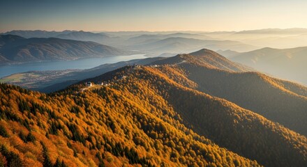 Golden autumn mountain range with a vibrant forest canopy. Aerial perspective of a scenic valley with a lake. Beautiful sunrise light over hazy hills