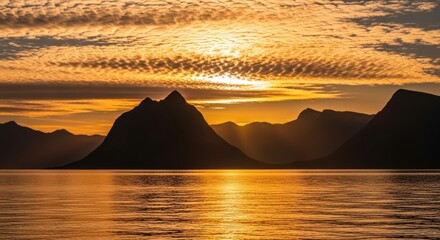 Golden hour sunset over a mountain range silhouette. Sun reflecting on the calm sea surface. Scenic nordic fjord landscape for travel and tourism. Concept of tranquility and natural beauty