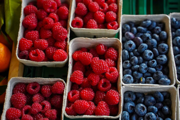 Raspberries and blueberries laying in the paper punnets  at the farm market