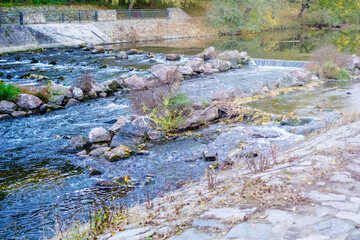 shallow river water flowing rapidly over a series of rocks and small weirs in a managed urban park stream with concrete banks, concept of engineering, ecology, water management