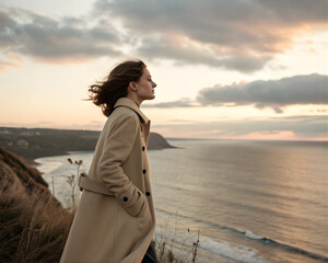 Fototapeta premium Woman standing on cliff overlooking ocean at sunset, peace and self-discovery, vast nature, romantic mood