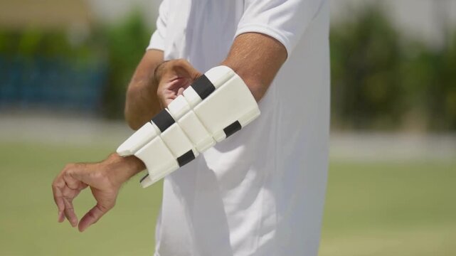 Close-Up Shot of Cricketer Wearing Elbow Pad &mdash; Athlete Preparing for Match, Putting on Protective Gear, Sports Safety Equipment, and Professional Cricket Player Readiness in 4K Ultra HD