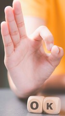 Child s hand forms ok gesture above wooden blocks spelling ok