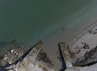 Straight down aerial view of concrete ramps or slipways leading into the calm, turquoise water on a rocky beach near dublin, ireland