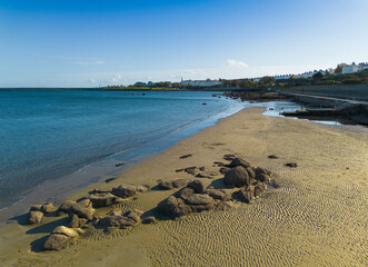 A beach with a rocky shoreline and a clear blue sky. The beach is empty and the rocks are scattered across the sand. Dublin Blackrock beach