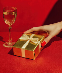 Female hand touching golden gift box with champagne glass	
