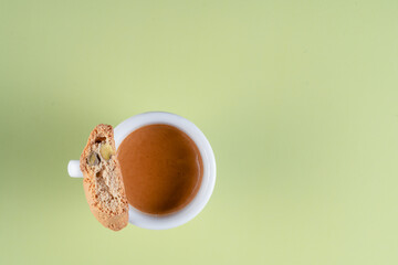 A cup of coffee with a biscuit on top. The biscuit is a crumbly pistachio biscuit