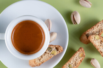 A rich espresso served with traditional Italian biscotti, featuring whole pistachio nuts, set against a vibrant green backdrop