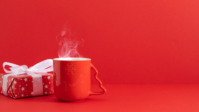Cozy Christmas mood: a steaming red mug with snowflakes and a festive gift box on a bright red background. Perfect for holiday banners and seasonal greetings.