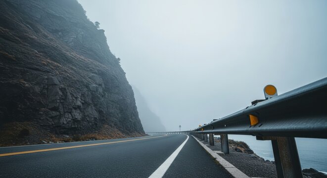 Coastal highway curving along a rocky cliff on a foggy day. Empty asphalt road for a scenic drive or road trip. Travel and adventure concept with a mysterious atmosphere - Powered by Adobe