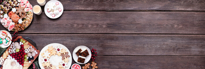 Christmas holiday cookies and sweets corner border. Above view on a dark wood banner background. Santa Claus grazing board, cookie platters and sweet plates. Copy space.