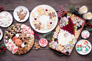 Christmas holiday cookies and sweets table scene. Top down view on a dark wood background. Santa Claus grazing board, cookie platters and sweet plates.