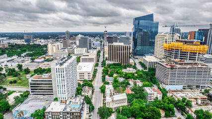 High-angle cityscape of Austin, Texas, showcasing a diverse architectural blend. Gleaming glass towers stand alongside historic buildings and construction cranes. A busy street cuts through the center