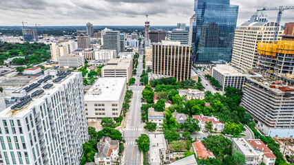 High-angle cityscape of Austin, Texas, showcasing a diverse architectural blend. Gleaming glass towers stand alongside historic buildings and construction cranes. A busy street cuts through the center