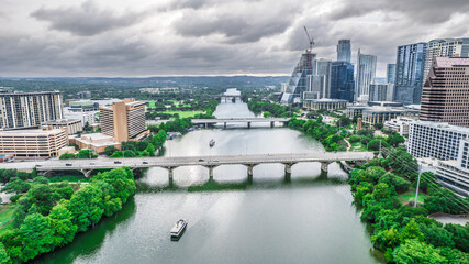 Panoramic aerial shot of Austin, Texas. The Colorado River flows beneath a bridge with city skyscrapers in the background under dramatic cloudy skies. Modern urban landscape, river views, Texas.