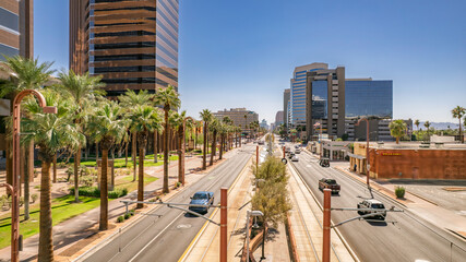 Vibrant street scene in downtown Phoenix, Arizona featuring palm trees lining a wide avenue with traffic and modern buildings. The sunny day creates a bright and energetic feel. Suitable for marketing