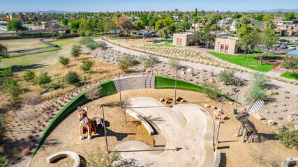 Drone shot of a modern skate park in Arizona. Kids playing, concrete ramps, sandpit, green landscaping. Great for recreation, youth, family, urban design.