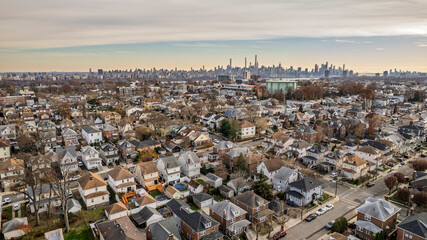 Panoramic aerial view of a residential neighborhood bathed in golden hour light. Houses line streets beneath a vibrant blue sky with wispy clouds. Urban landscape, suburban serenity, peaceful