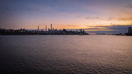 Dramatic sunset over the East River in New York City. The iconic skyline is silhouetted against a vibrant orange and purple sky. Perfect for cityscapes, travel, or romantic themes