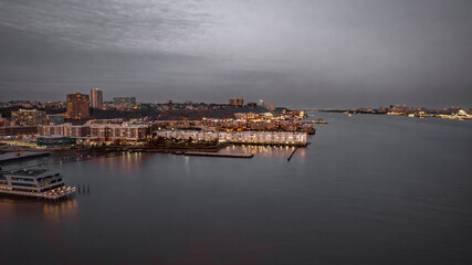 Nighttime cityscape view. Illuminated buildings reflect on calm water. Dramatic sky adds depth to...