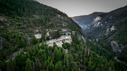 Dramatic Yosemite Valley landscape at sunrise. Golden light illuminates granite cliffs amidst lush evergreen forests. Stunning mountain vista. High resolution.