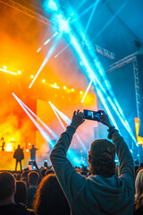 A concertgoer films a vibrant stage performance on their smartphone amidst a lively crowd
