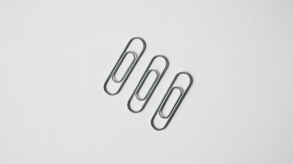 Obraz premium Three Silver Paperclips in a Diagonal Row on a White Surface office supply stationery