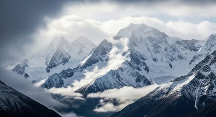 Obraz premium Snow capped mountain peaks in dramatic light. Stormy clouds and mist in an alpine valley. Concept for overcoming challenges and success. Adventure travel and wilderness exploration