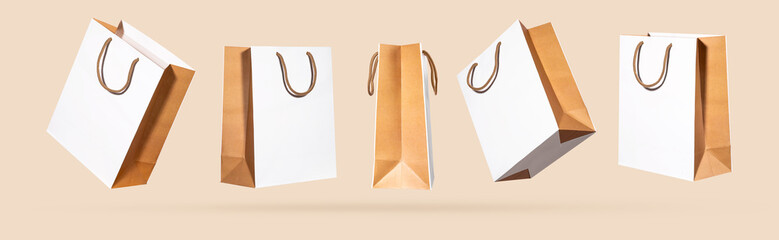 White beige paper shopping bags flying from different sides, light pastel background. Creative concept shopping discounts, sale purchase in store. Cut out template objects for design. Mock up. Banner