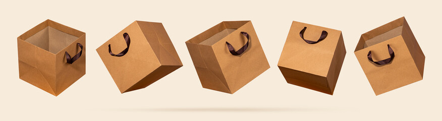Five square kraft paper shopping bags flying on light beige background. Concept eco-conscious...