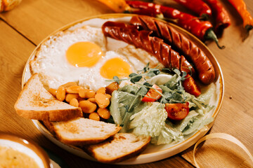 Delicious breakfast plate with eggs, sausages, salad, and toast on wooden table