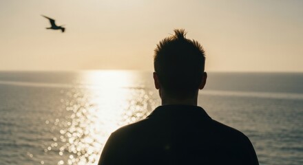 Male silhouette watching a golden sunrise over the ocean. Contemplative man thinking about the future. Freedom and hope concept with a flying bird. Personal journey and mental clarity