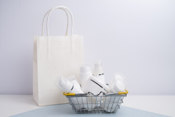 Miniature basket filled with white, unlabeled cosmetic bottles on a minimalist background. Beauty...