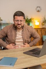 Disappointed Caucasian male freelancer feeling overeating during work process on laptop in home...