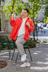 Asian middle-aged man shouting celebrating success winning goal achievement good news lottery jackpot casino luck victory career outdoors. Chinese guy on urban city street. Town lifestyles. Vertical