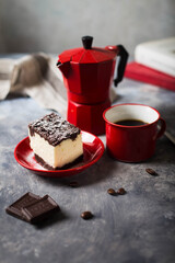 Cheesecake with chocolate base served with coffee in red cup and small coffee pot.