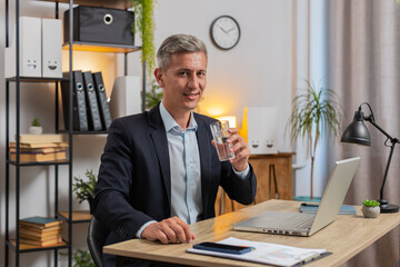 Focused Caucasian businessman sitting at workplace desk drinking water while working with laptop in...