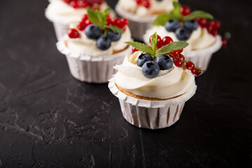 Delicious vanilla cupcakes decorated with mascarpone cream and berries (blueberries, currants, mint)