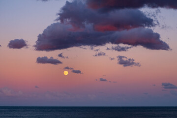 Yellow full moon above calm sea under violet pink twilight sky with scattered clouds creating serene atmosphere of peace balance and wonder symbolizing harmony between nature and cosmos