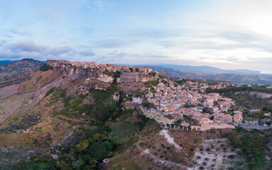 Aerial view: ancient village of Gerace Calabria Italy built on rocky mountain top at sunrise with dramatic cliffs and historic stone houses symbolizing heritage and Mediterranean culture