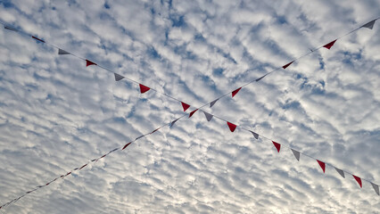 Scenic view of red and white triangular bunting flags crossing in the sky with a beautiful pattern of altocumulus clouds in the background