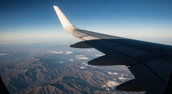 Aerial view from an airplane window showing the wing. Commercial flight over a mountain landscape. International travel and business transportation concept. Journey and adventure in the sky
