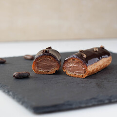 Elegant french chocolate eclairs decorated with chocolate shiny glaze and cocoa beans served on black slate board 