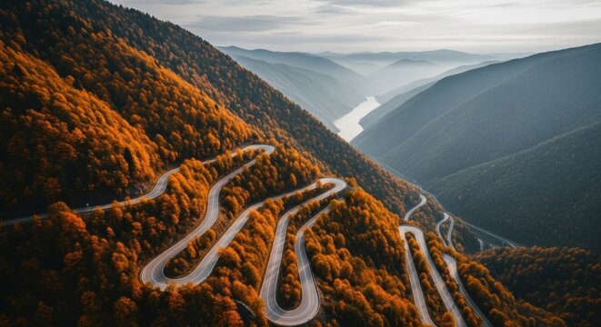 Winding mountain pass during autumn season. Aerial drone perspective of a scenic highway. Transportation route through a vibrant orange forest. The journey to success concept - Powered by Adobe