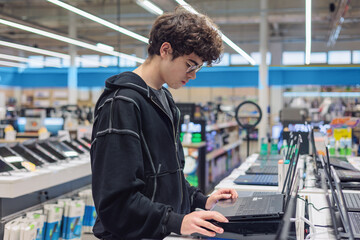 Teenager Choosing a Laptop in Electronics Store – Young Customer Testing Computers, Tech Shopping, Retail Consumer Behavior, Gadget Choice.  digital lifestyle, gadget choice. technology purchase